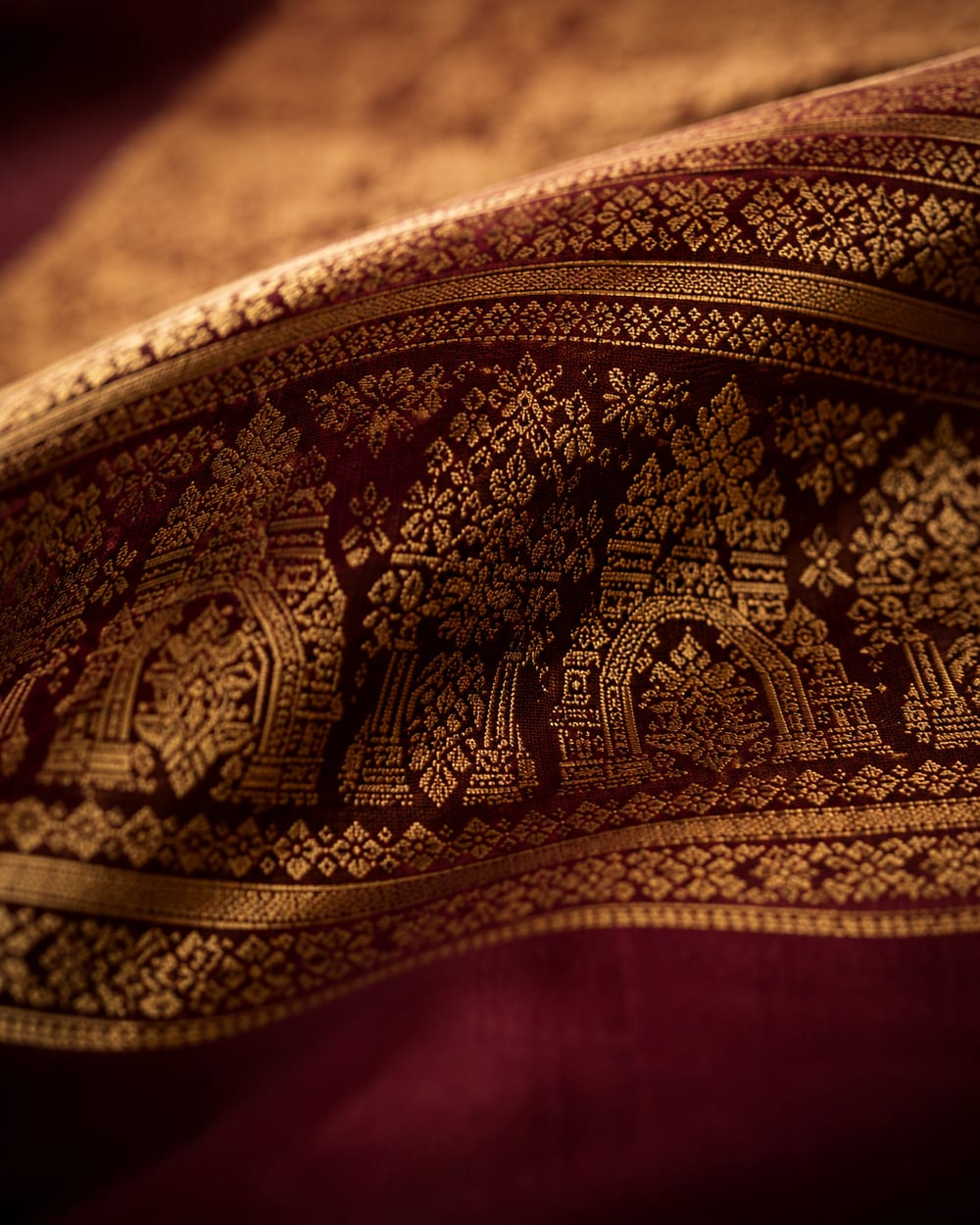 Artisan hands weaving gold zari into maroon silk